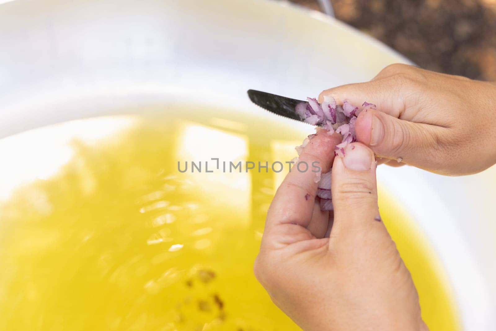 Woman hands chopping red onion over a big frying pan with olive oil close up, copy space. Traditional italian and apulian cousine, cooking for huge family