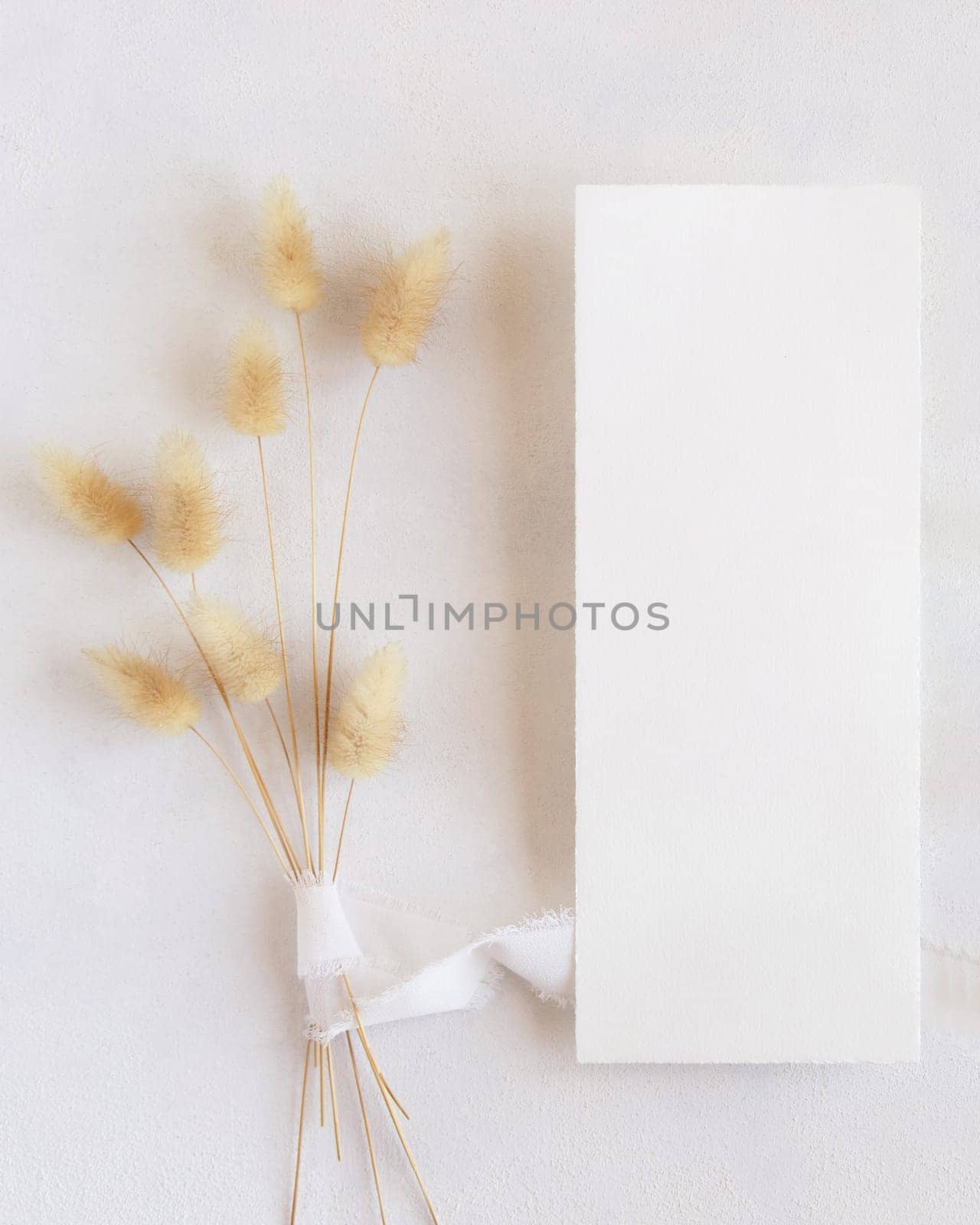 Blank card near silk ribbons and dried hare's tail grass top view on white, mockup. Boho romantic scene with vertical card. Bohemian or close to nature greeting or wedding Invitation
