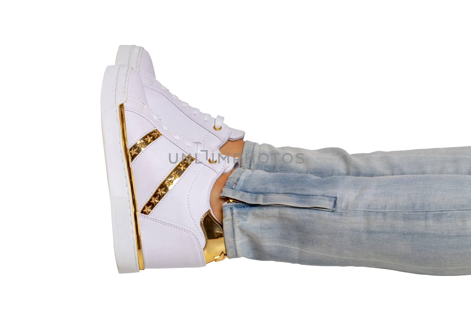 Women legs in jeans and sneakers. Woman legs in light denim pants wearing modern white sneaker. Fashionable white footwear. Clipping path. Macro photograph.