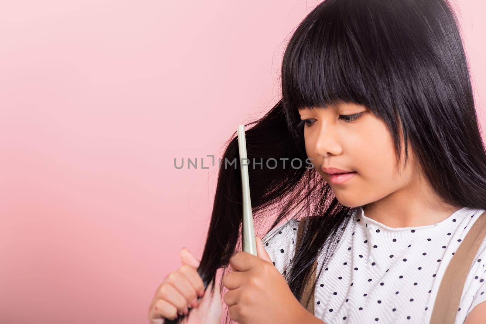 Asian little kid 10 years old hold comb brushing her unruly she touching her long black hair at studio shot isolated on pink background, Happy child girl with a hairbrush, Hair care concept