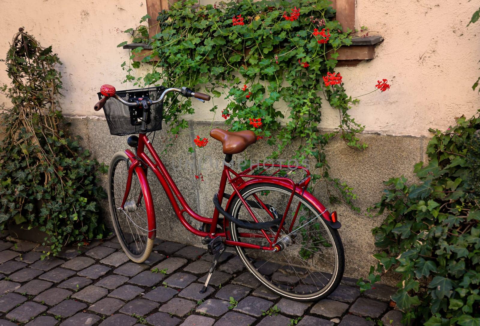 A bright red ladies bike with basket on a house wall.