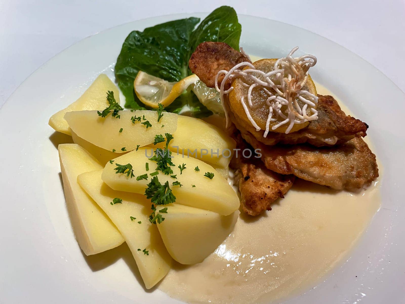 Fish with potatoes and lemon sauce on a plate.