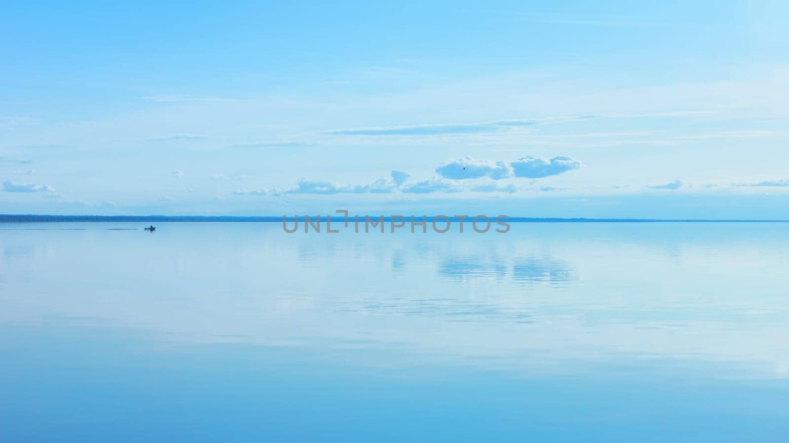 Light blue sky reflected in a calm smooth lake surface. Atmosphere of serenity and tranquility. Summer seascape background with space for copy. Russia, Vologda Oblast, Lake Beloye.