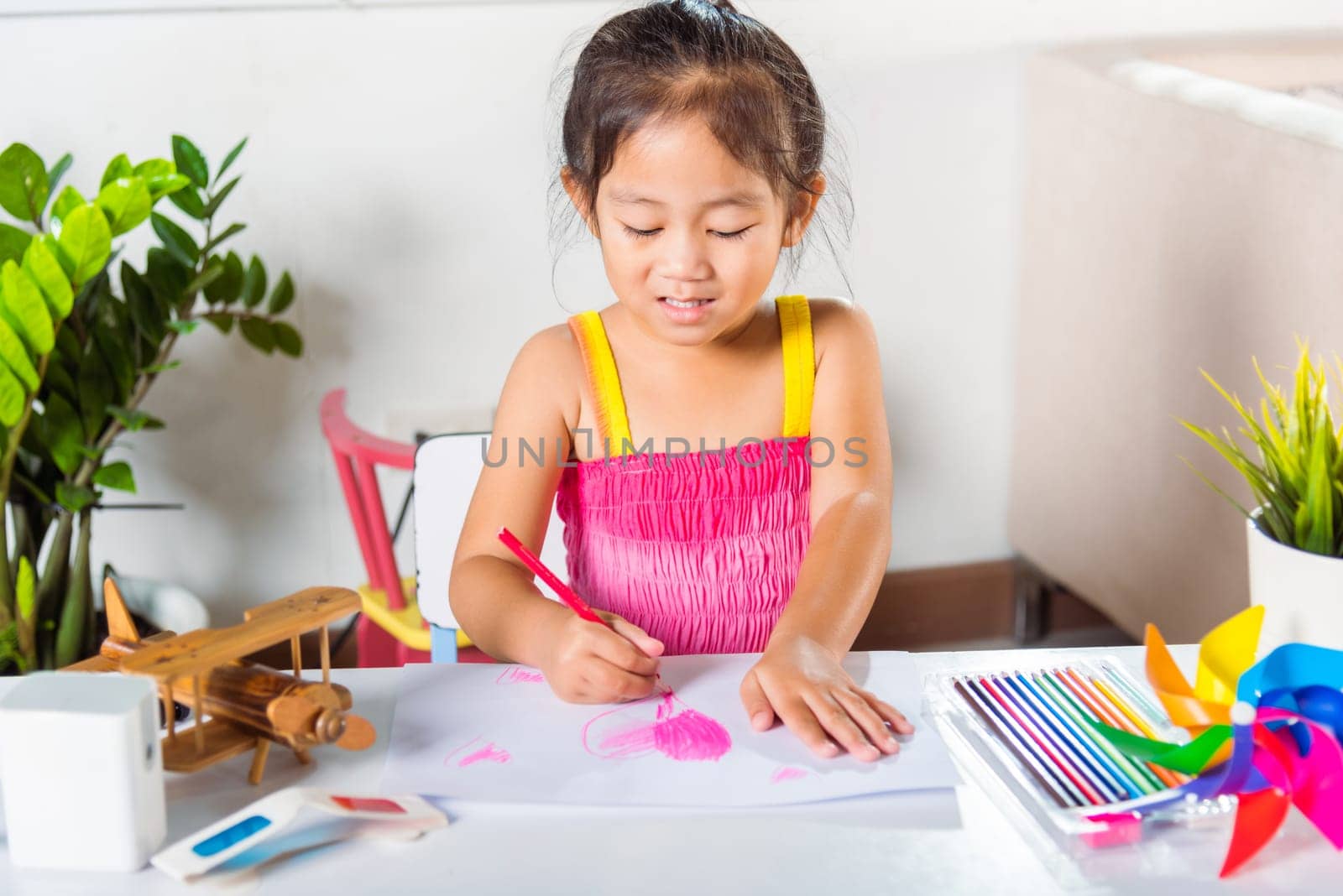 Happy child little girl colorful drawing pink heart on white paper, Asian cute kid preschooler smiling draw color love picture card at home, Valentine's or Mother's Day or Father's Day
