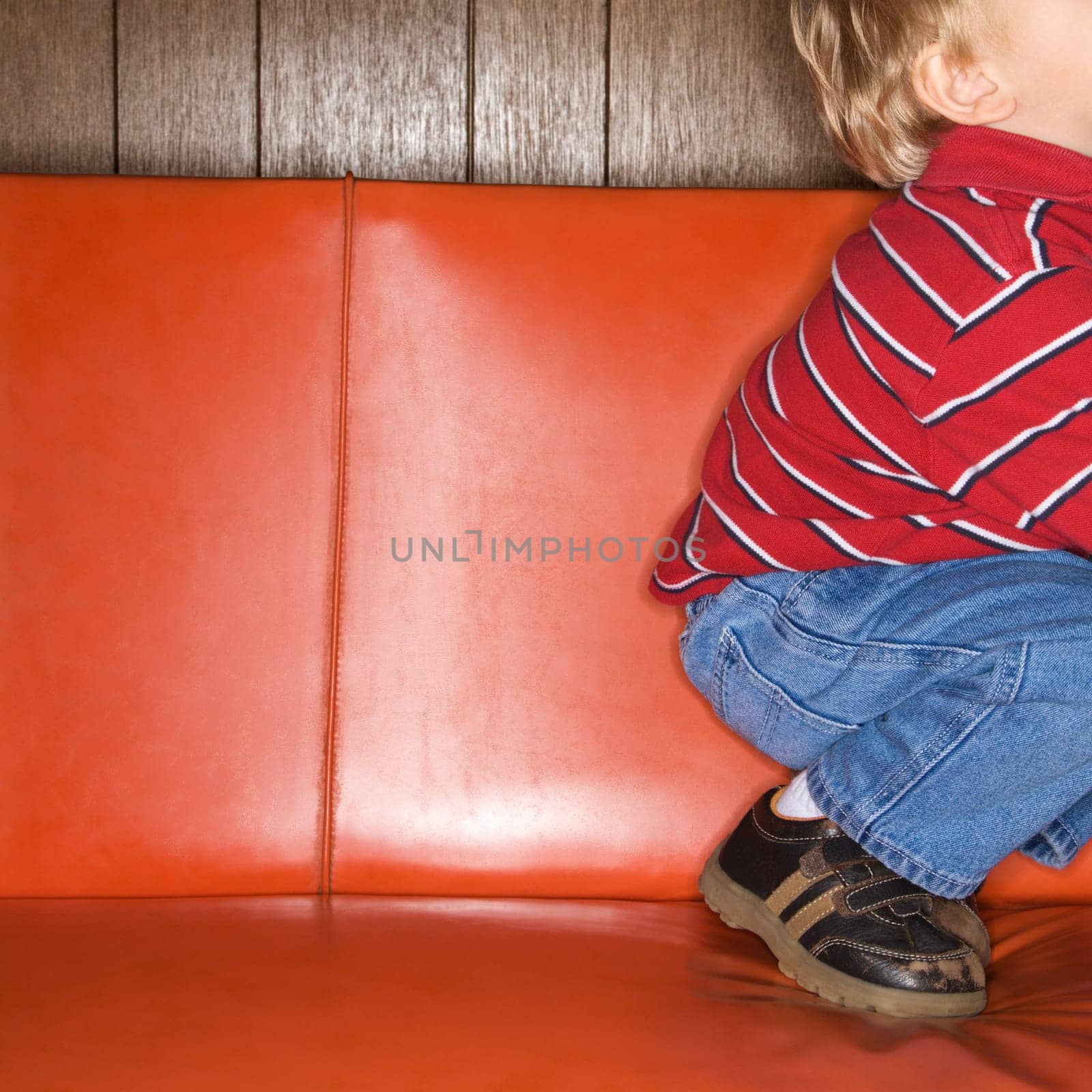 Caucasian boy kneeling on vinyl sofa.