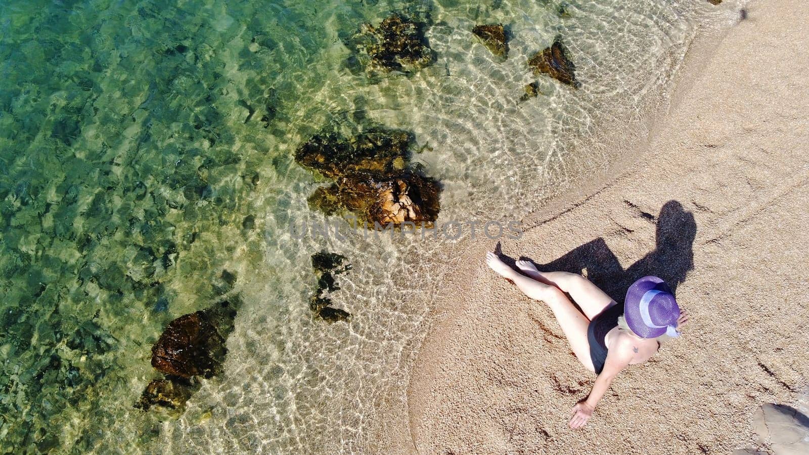 Woman in swimsuit and straw hat sits in the sand by the sea