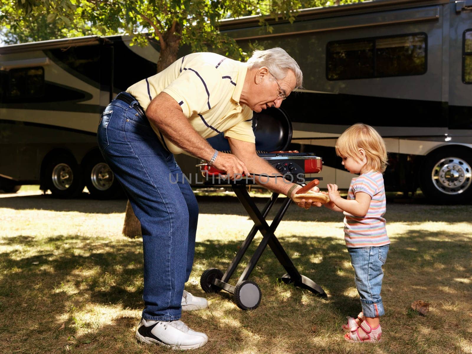 Grandfather giving granddaughter hotdog by RV.