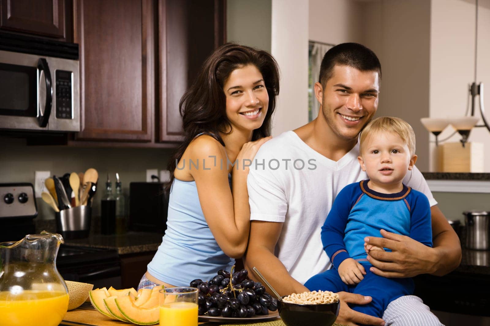 Caucasian family with toddler son in kitchen at breakfast smiling at viewer.