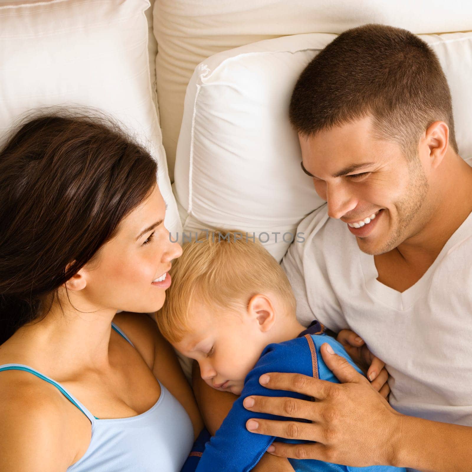 Caucasian mid adult parents with toddler son sleeping in bed.