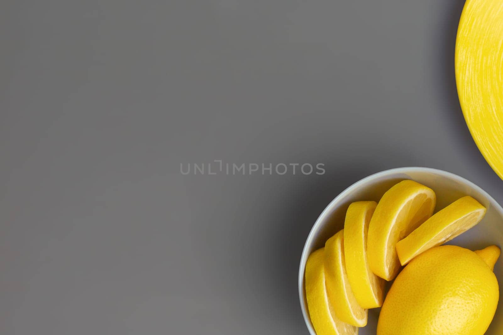 Yellow lemons in gray plate on gray background. Colors of the Year 2021 Pantone Illuminating and Ultimate gray. Flat lay. Copy space