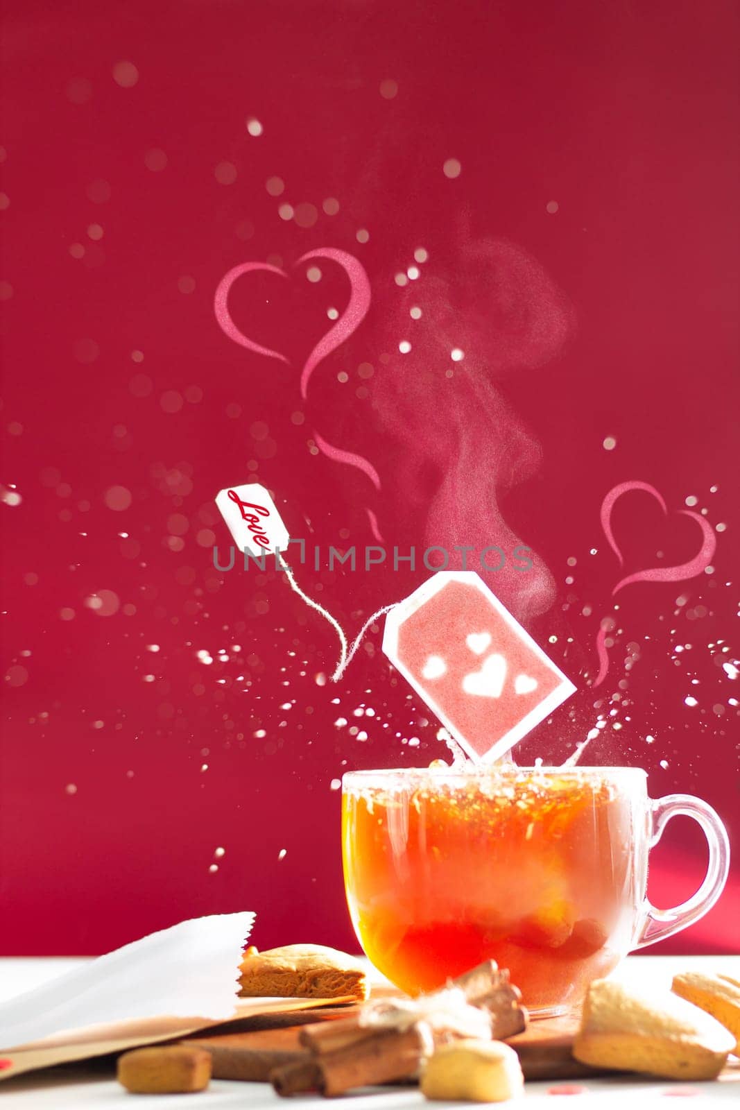 Tea bag with hearts and inscription Love on label above tea mug with splashes and heart shaped steam on dark red background. Copy space