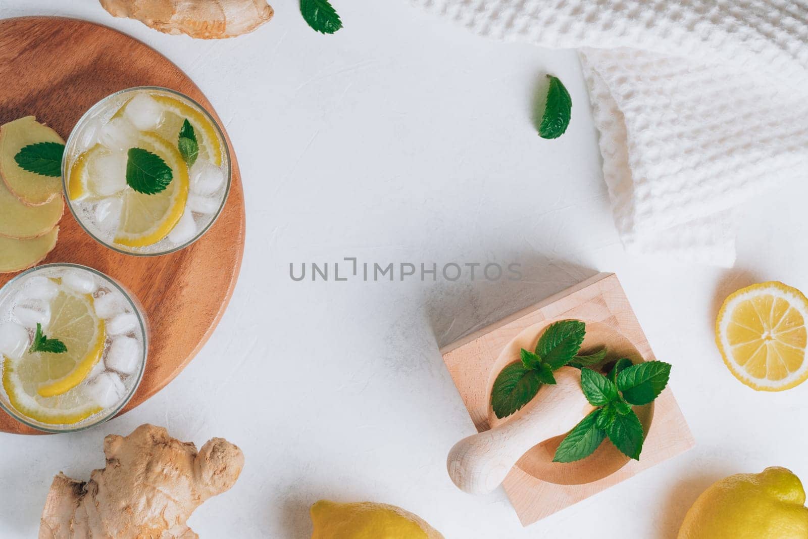 Two glasses with lemonade and ingredients for cooking. Ginger, lemon, mint, ice on white surface. Wooden tray, mortar and pestle. Flat lay. Copy space