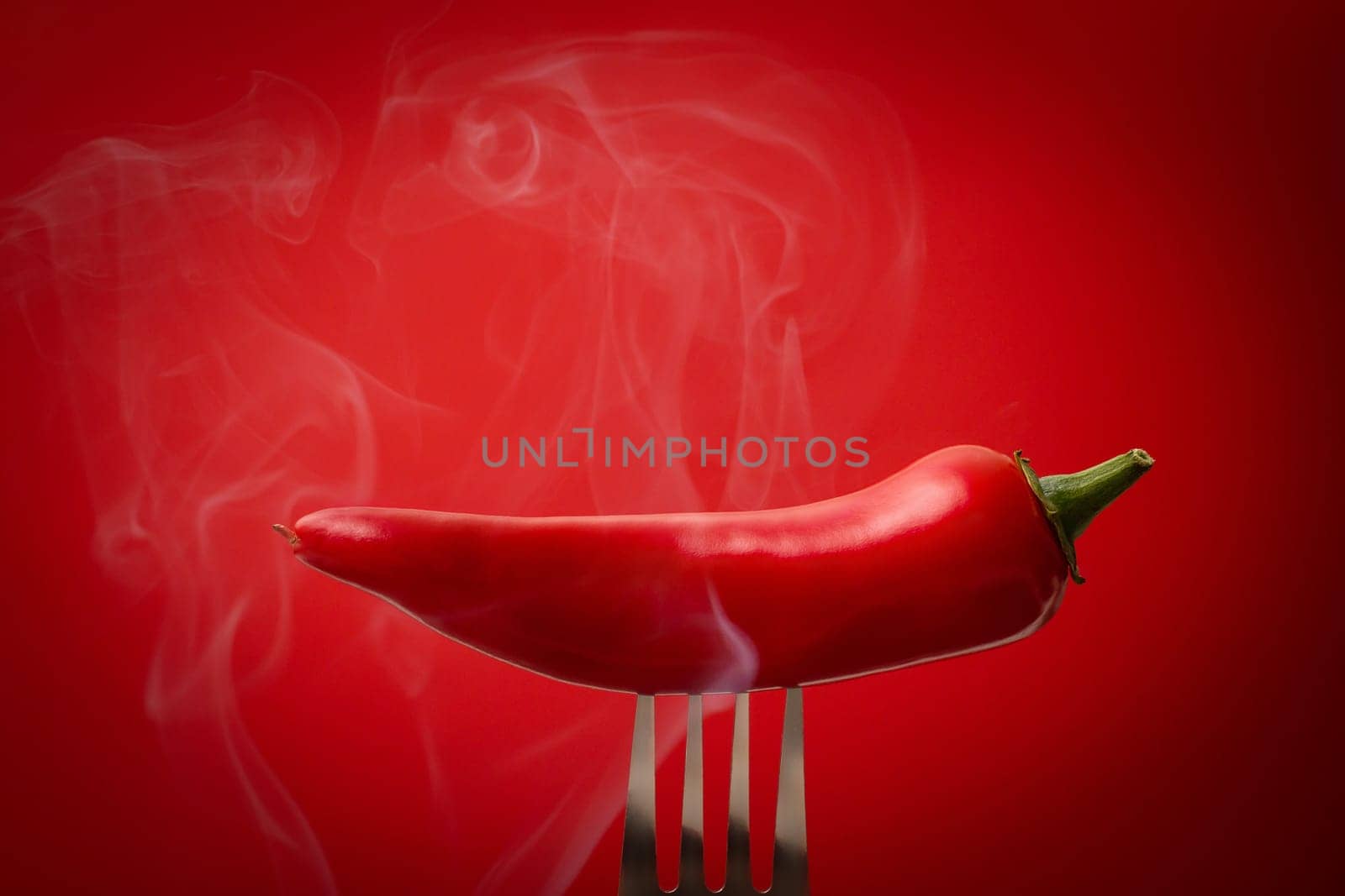 Steaming red pod of red hot jalapeno peppers on a fork on red background. Copy space