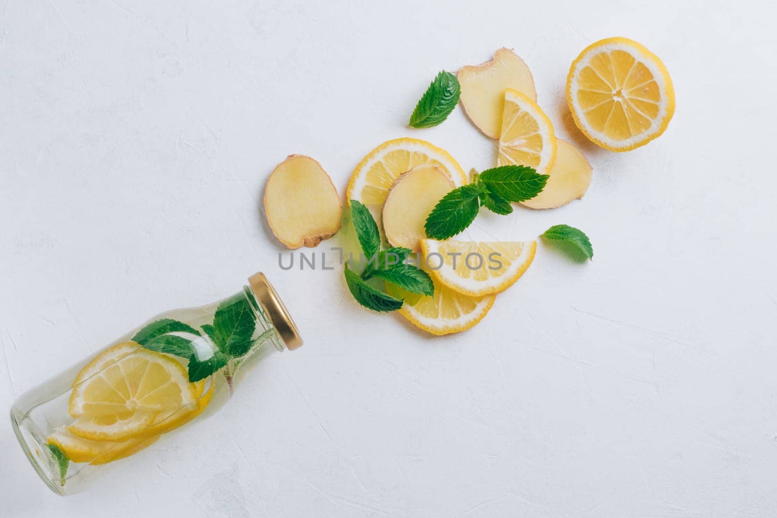 Glass bottle with lemonade and ingredients for cooking. Ginger, lemon, mint on white surface. Flat lay, top view