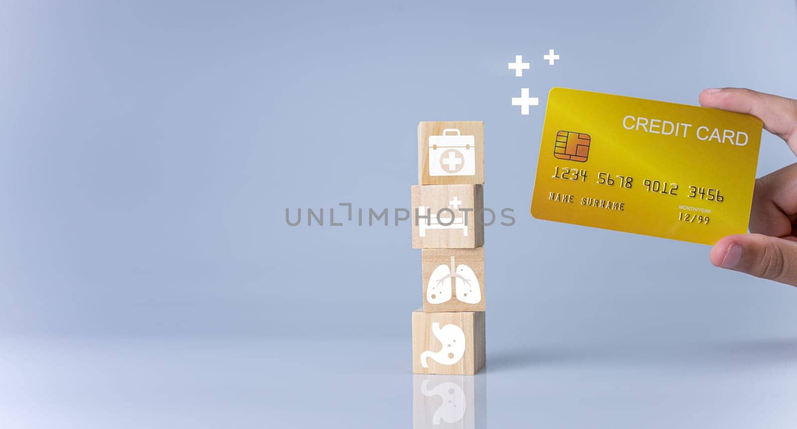 Hand holding credit card and wooden cube blocks stacked with icons. Concept of medical expenses, health and medicine.