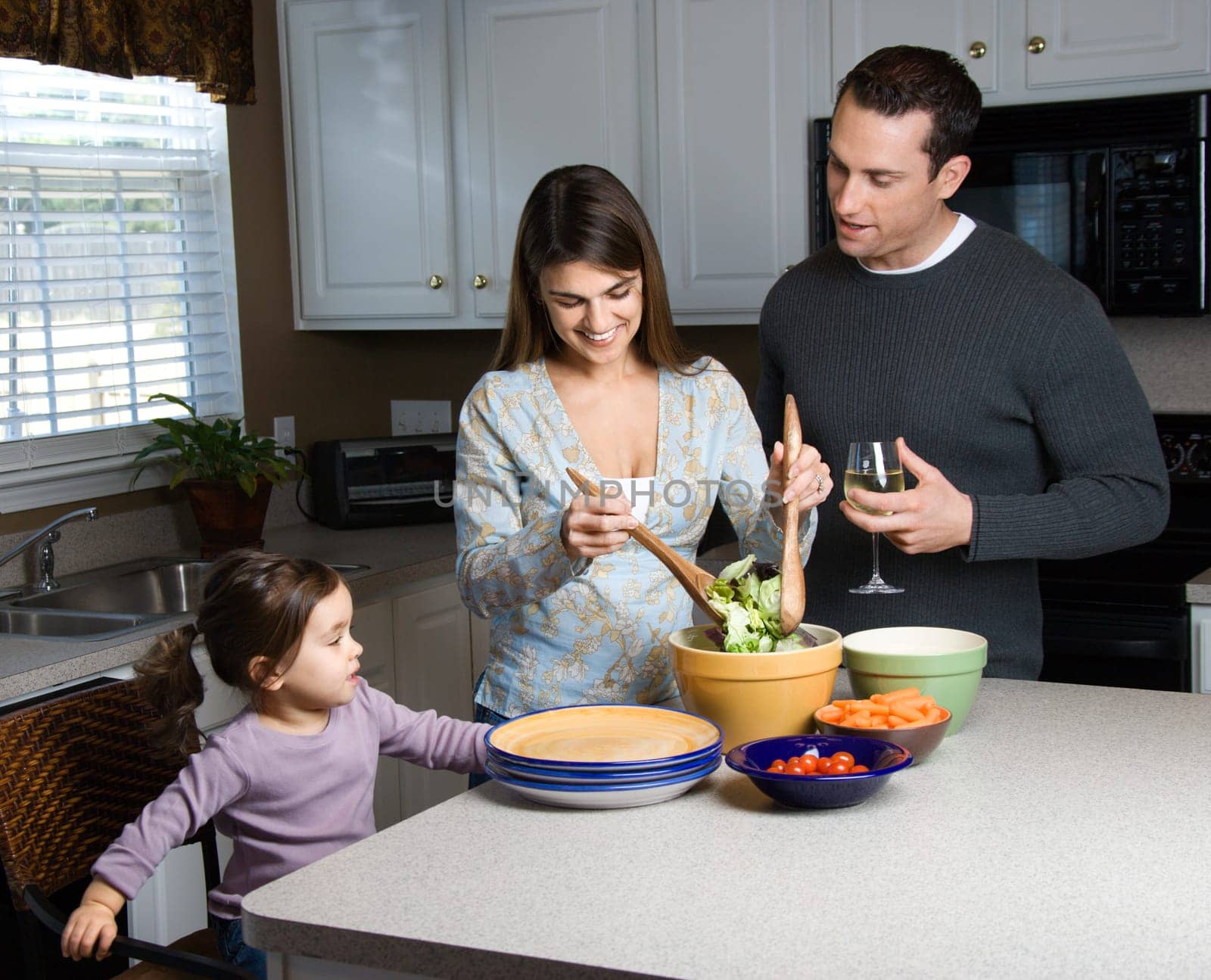 Caucasian woman making salad on kitchen counter with daughter and husband.