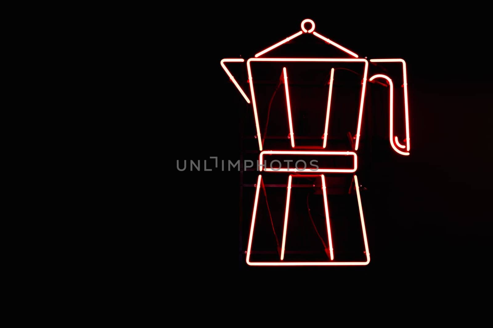 Red neon sign from lamps in the form of a Moka pot coffee maker on the wall of a black coffee shop.