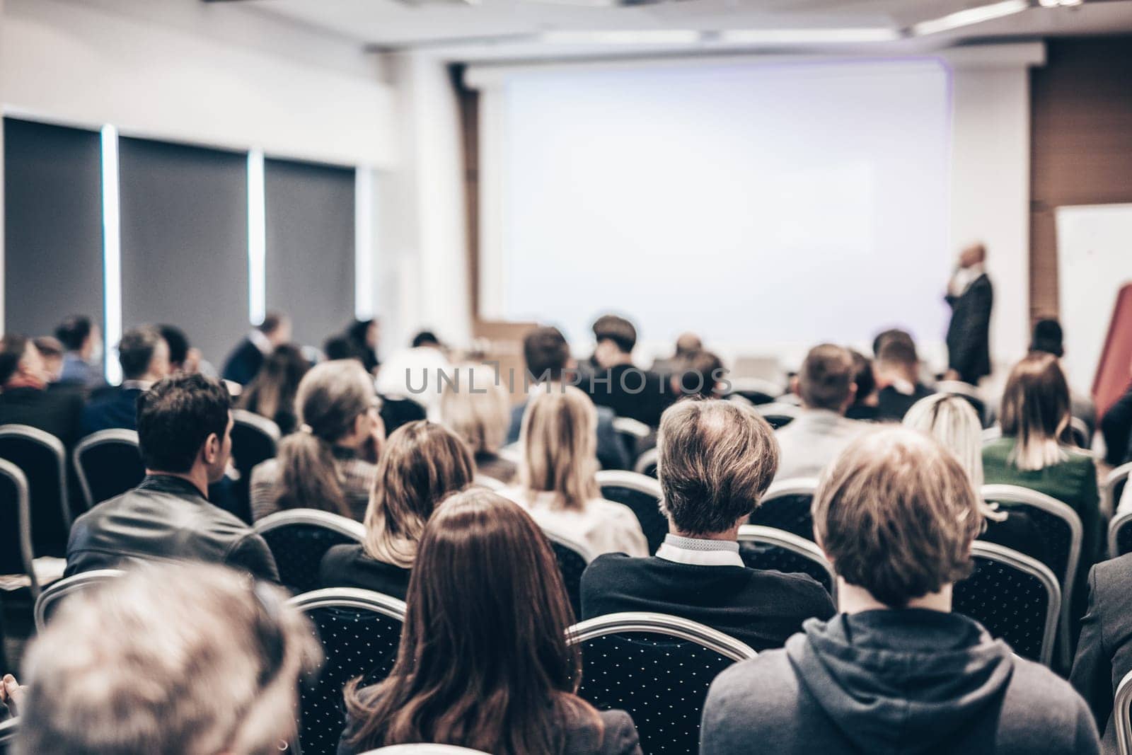 Speaker giving a talk in conference hall at business event. Rear view of unrecognizable people in audience at the conference hall. Business and entrepreneurship concept