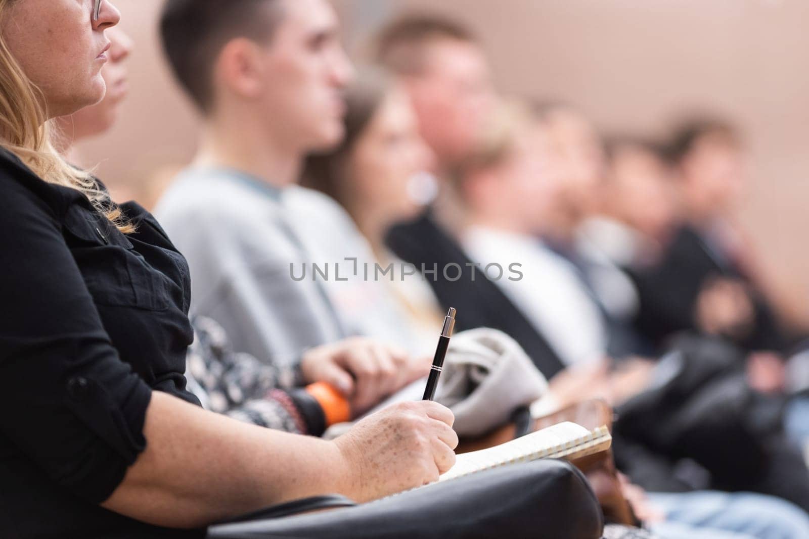Female hands holding pen and notebook, making notes at conference lecture. Event participants in conference hall