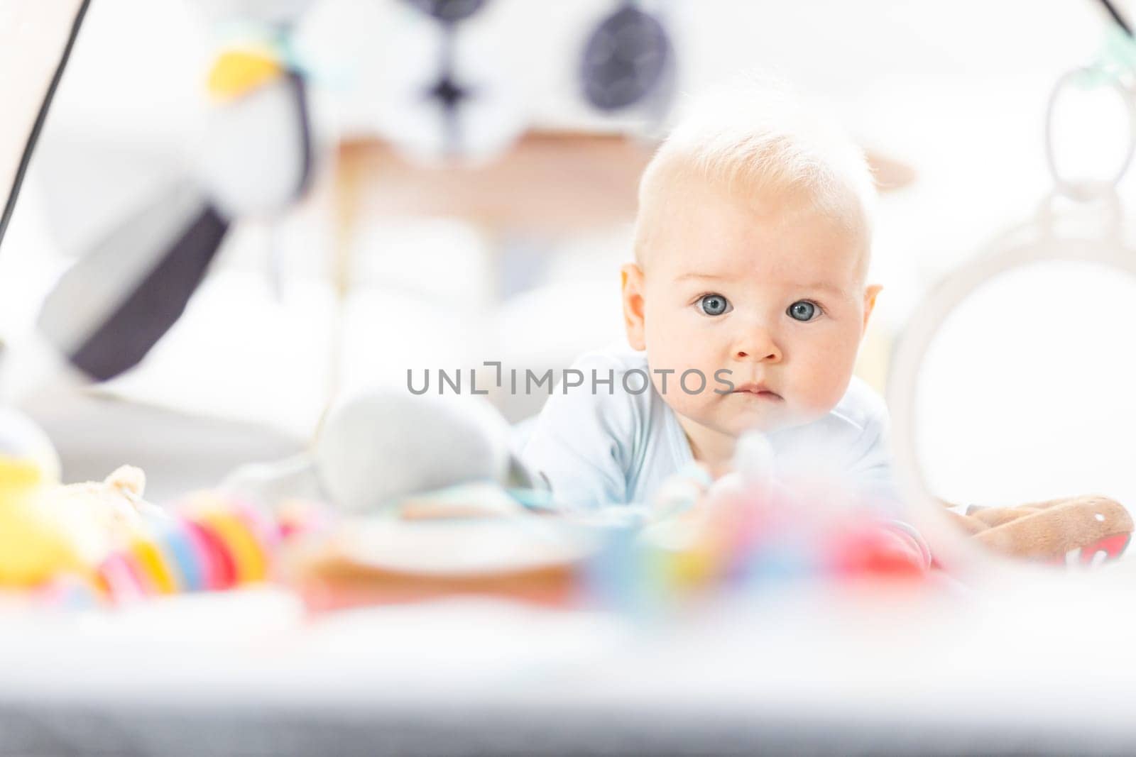 Cute baby boy playing with hanging toys arch on mat at home Baby activity and play center for early infant development. Baby playing at home.