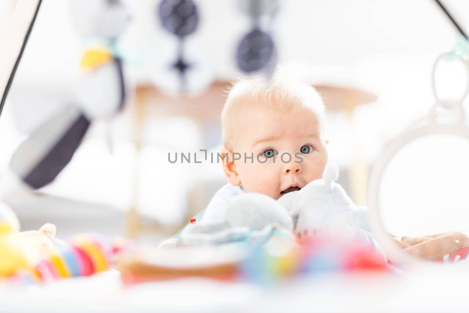 Cute baby boy playing with hanging toys arch on mat at home Baby activity and play center for early infant development. Baby playing at home.