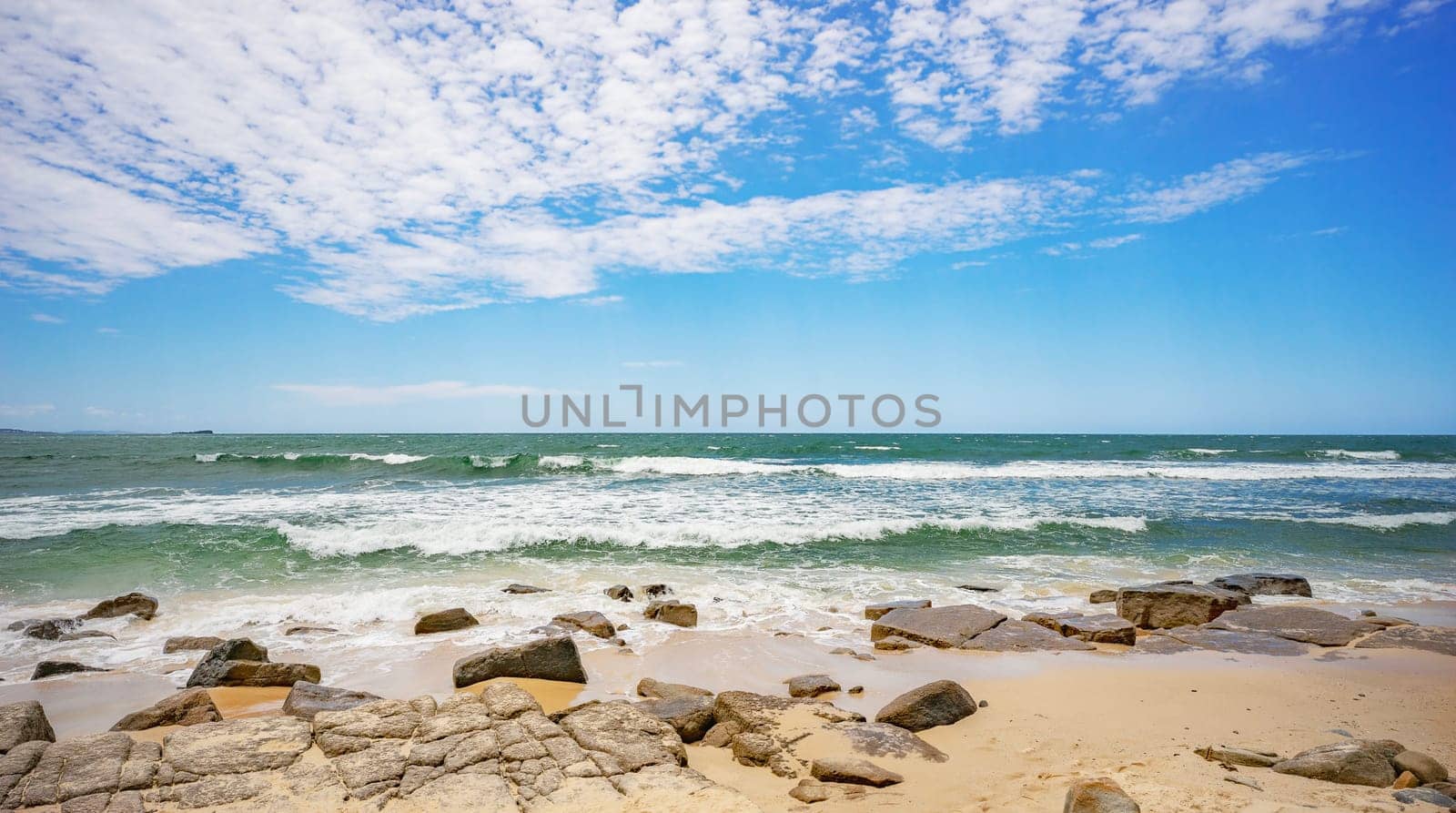 Looking out to the horizon of the Pacific Ocean from Alexandra Headland, Maroochydore. The sky is blue with inspiring white clouds, the ocean water is green with white breaking surf and the shoreline is sandy and rocky.
