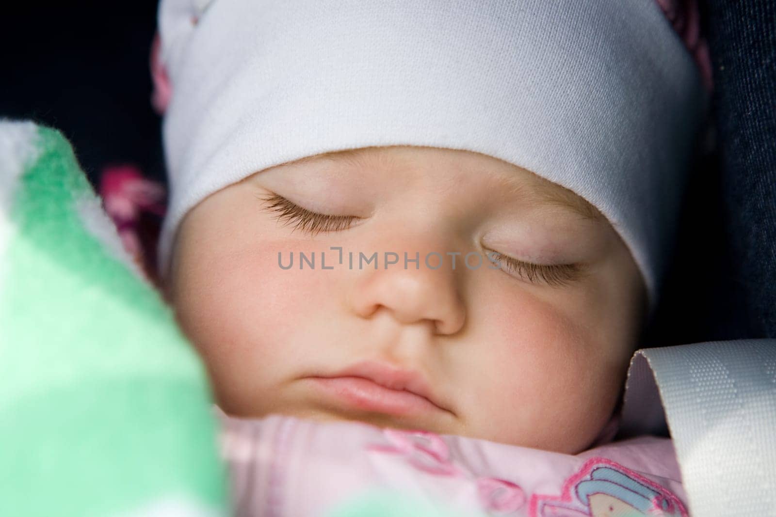 A portrait of the sleeping beautiful little girl in a white scarf close up.