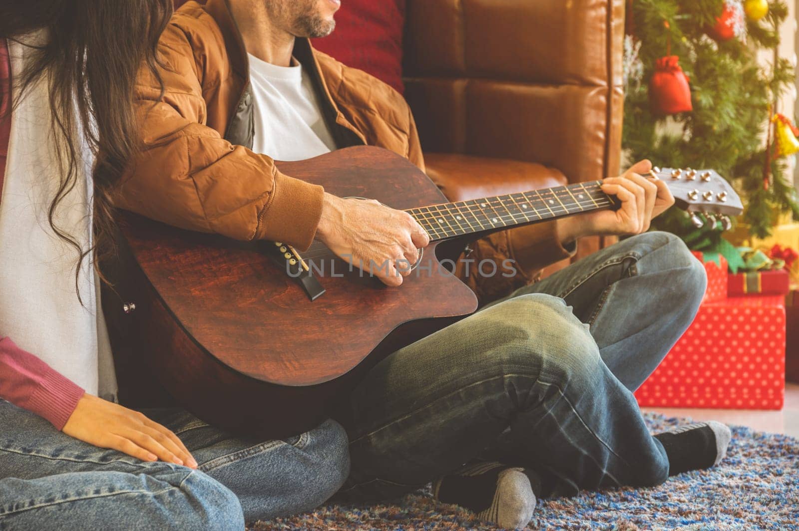 Happy cheerful couple enjoying great time in living room with guitar in Christmas holidays. Man playing guitar and singing for woman on carpet floor