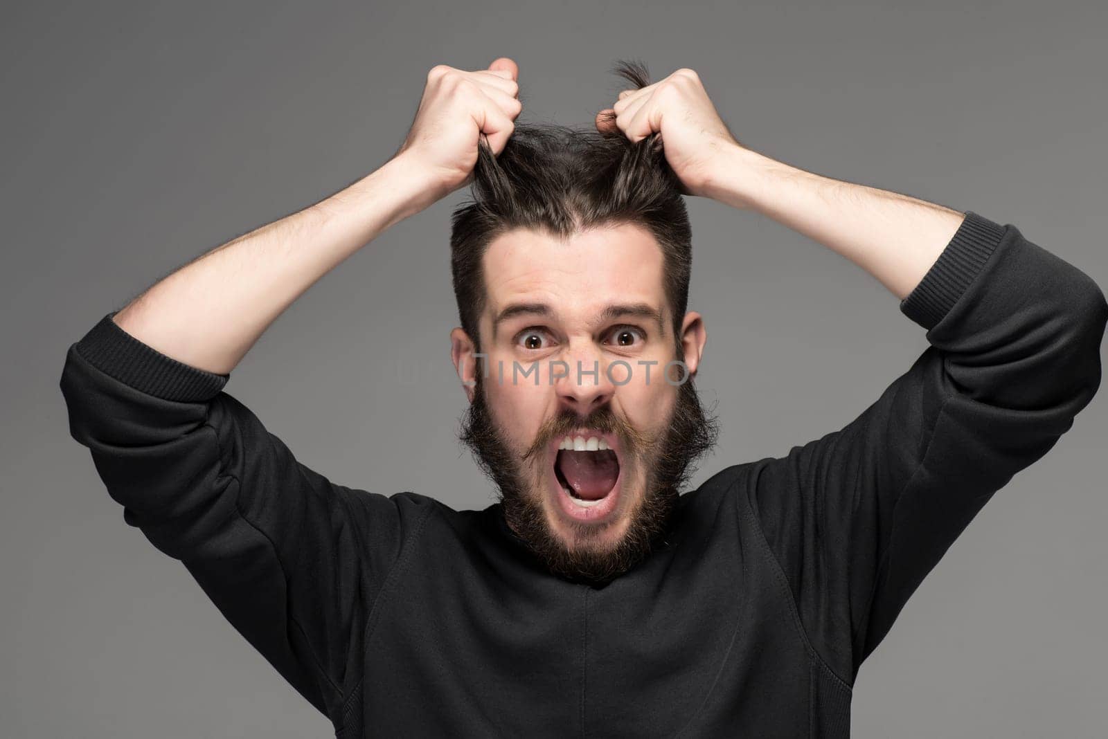 frustration, man in a black sweater tearing hair out in anger. portrait on gray background