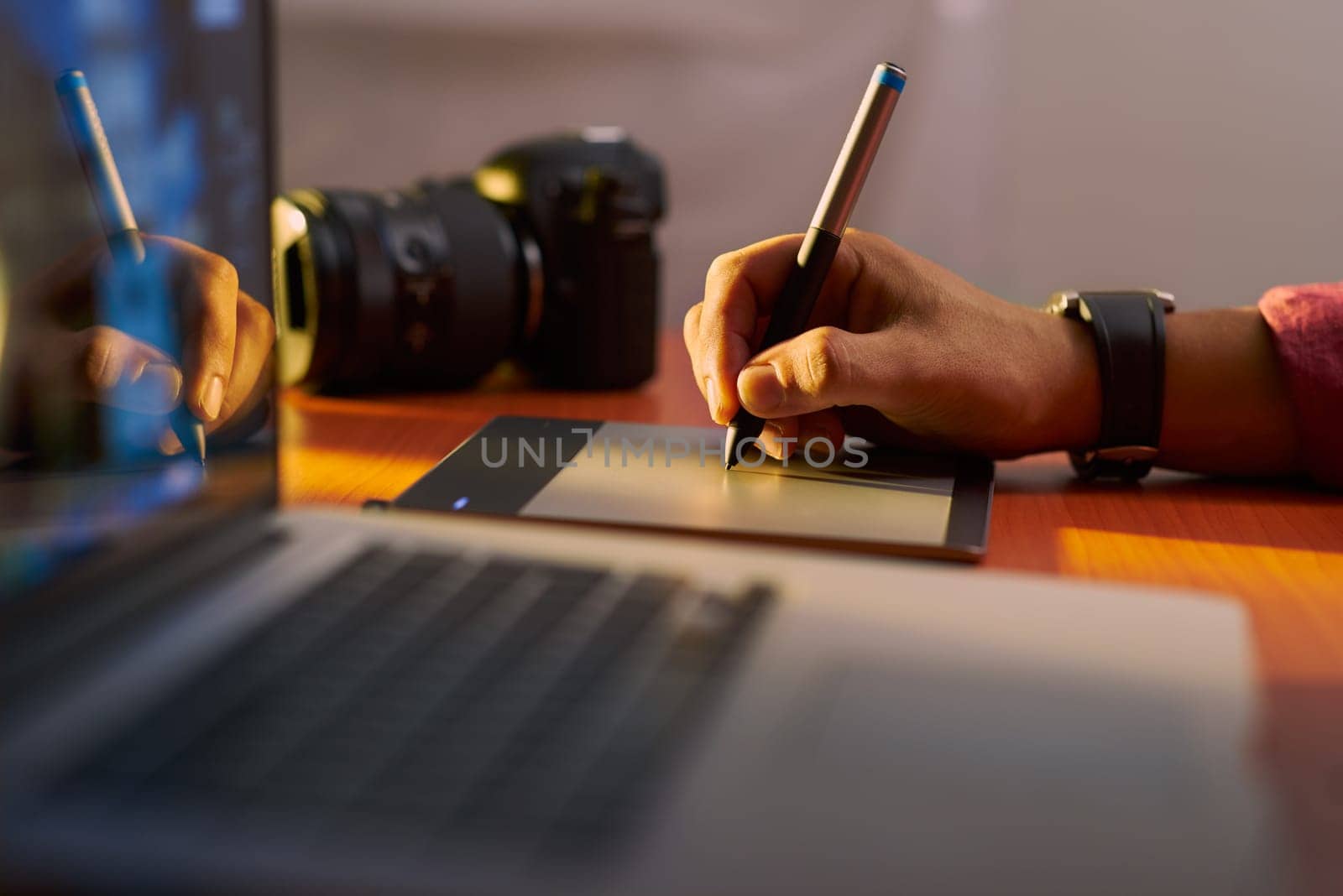 Photographer drawing and retouching image on laptop computer, using a digital tablet and stylus pen. Closeup of man's hand with dslr camera in background. Copy space in foreground