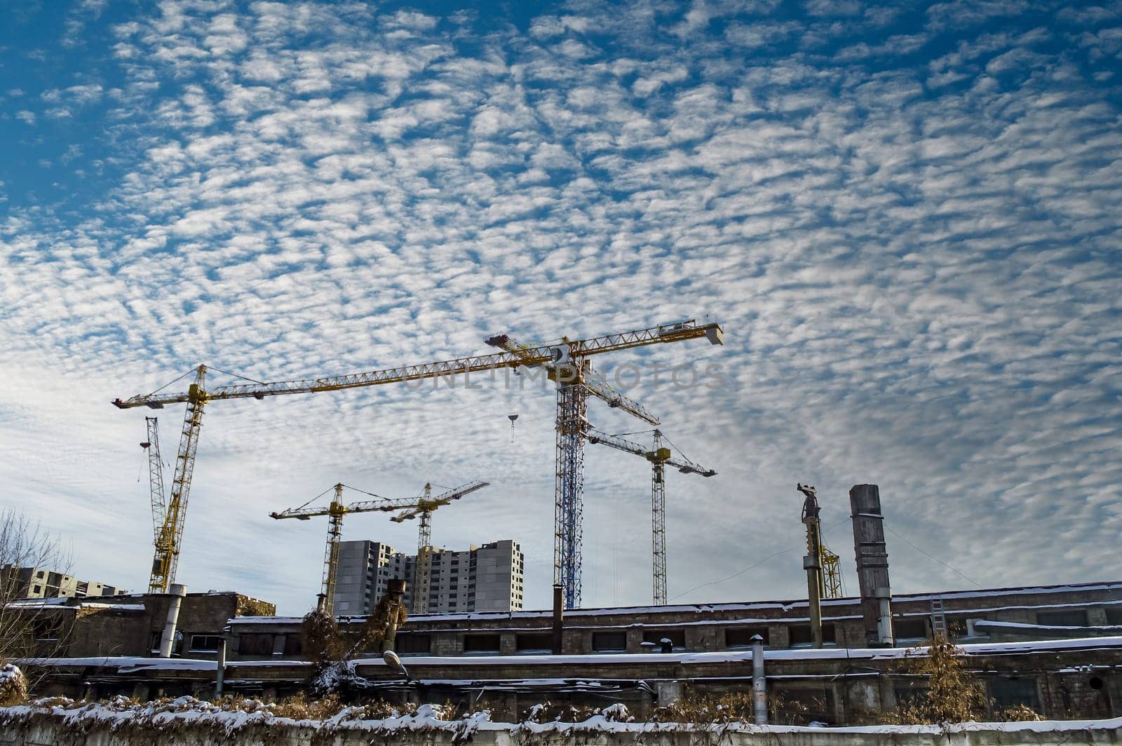 High-rise cranes are building a new house. Construction high-rise crane. New houses. Industrial landscape. Multi-storey building. Blue sky with white cumulus clouds. City life.