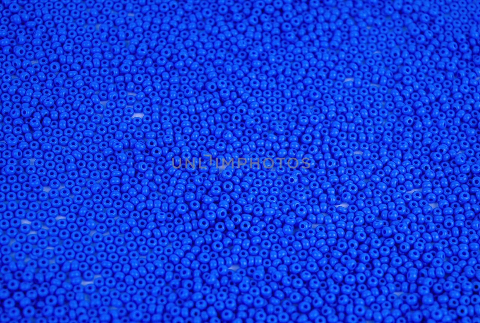 The texture of the surface of scattered blue beads for needlework. Beads for women's needlework. Blue round granules. Textured effect. Background image. Template for text.