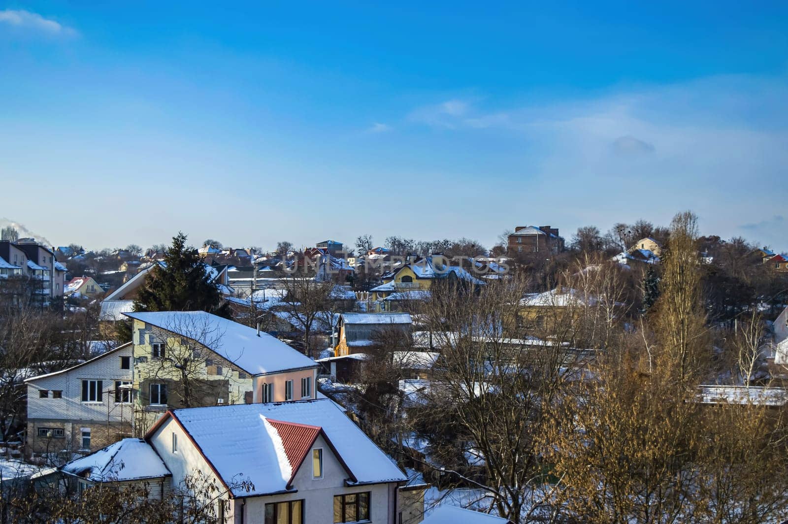 Snow-covered roofs of rural houses against the blue sky. Rural houses. Winter season. Blue sky. Cumulus clouds. White sneh. Cloudy horizon. Winter landscape. Background image.