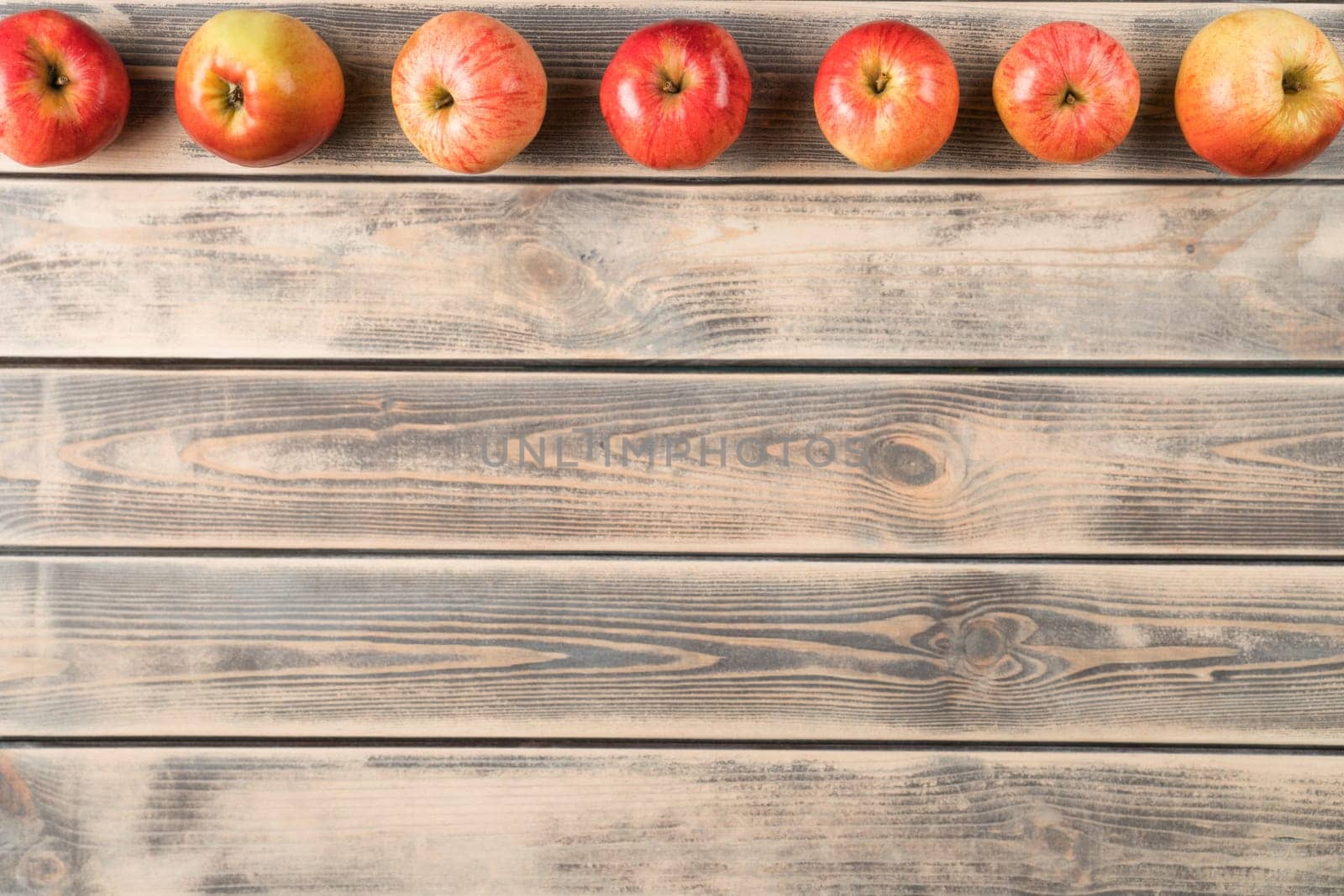 Horizontal line of fragrant sweet red apples on faded wooden table, top view. Fresh appetizing garden fruits arranged in order. Organic food or healthy diet concept. Planking. Place for text.
