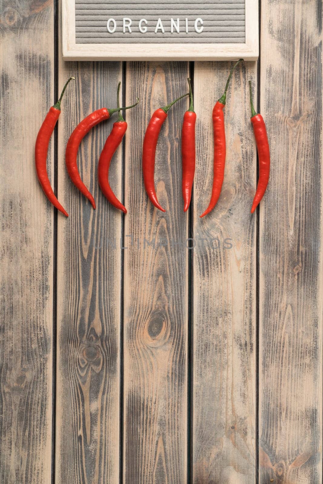Horizontal line of red hot peppers on faded wooden table, top view. Spicy chillies arranged in order. Organic food or healthy diet concept. Location of objects. Planking. Place for text.