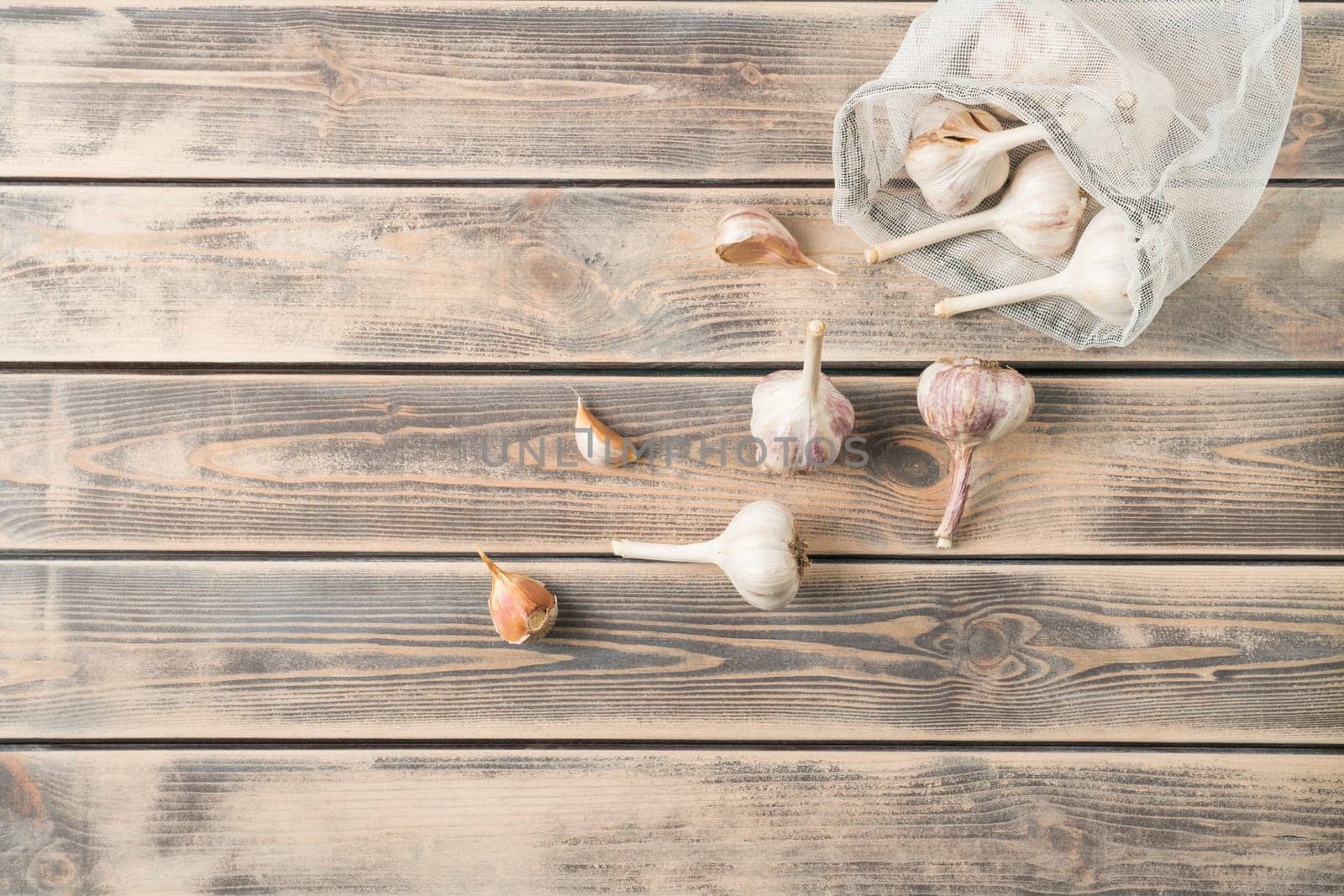Bunch of unpeeled garlic on faded wooden table, top view. Eco fabric poach full of aromatic spice. Food or healthy diet concept. Separated location of garlic cloves. Planking. Culinary and cooking.