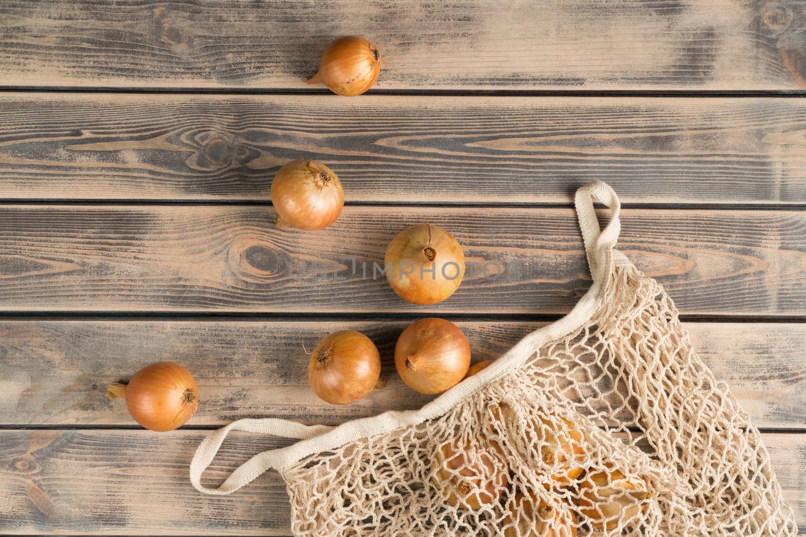 Bunch of unpeeled white onions on faded wooden table, top view. Farm vegetables take out from eco fabric mesh bag. Food or healthy diet concept. Separated location. Planking. Culinary and cooking.
