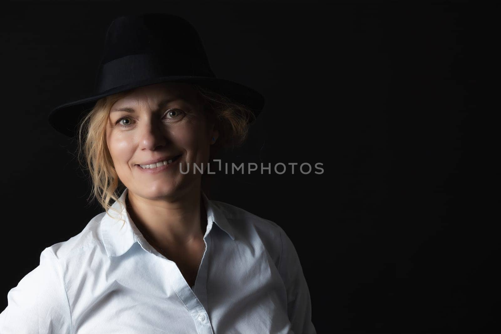 Low key portrait of smiling middle age woman wearing a black hat.