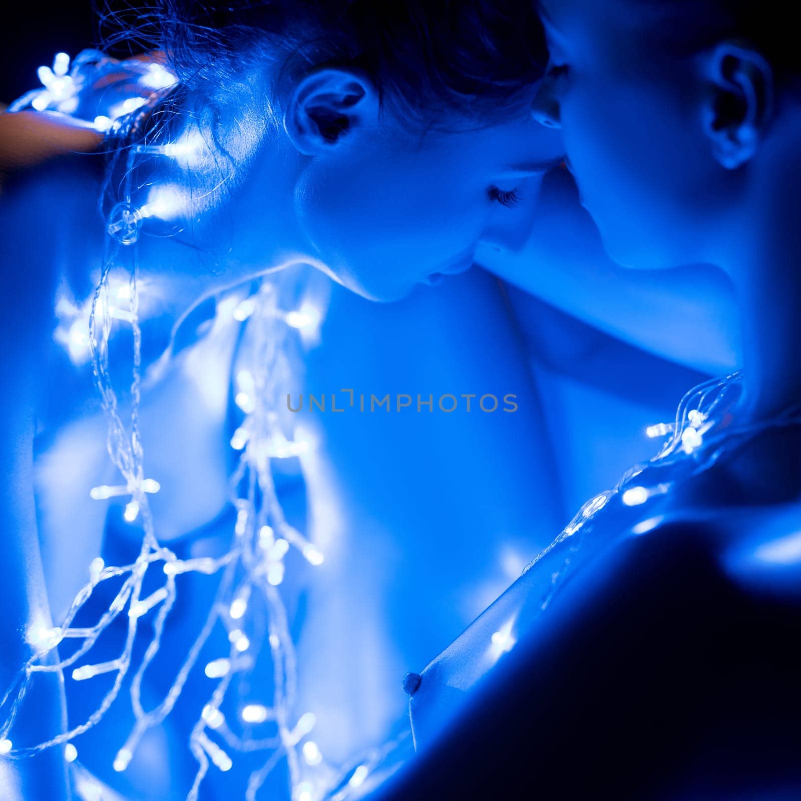 Two figures, adorned with glowing blue lights, lean close together, creating an intimate and captivating atmosphere.