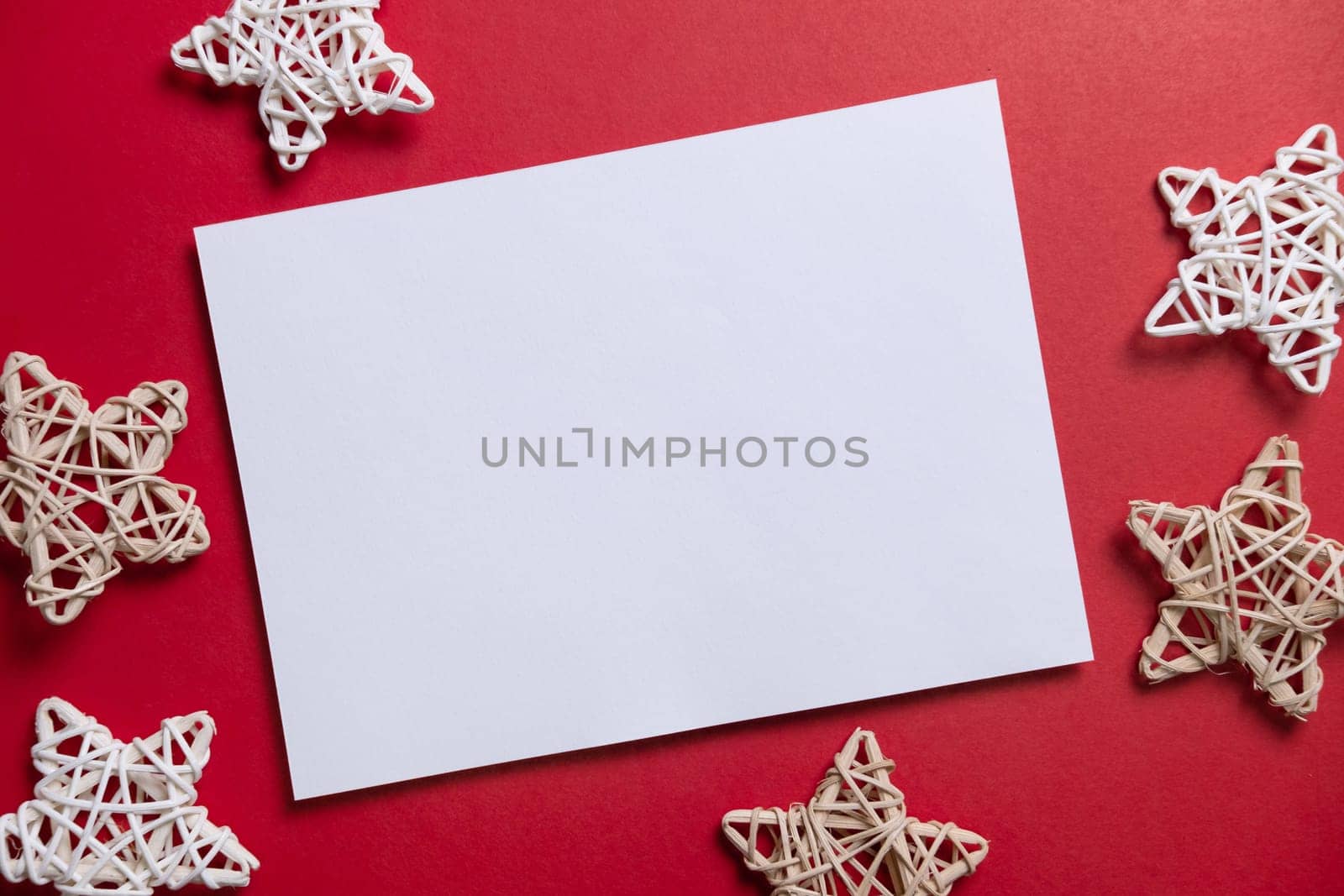 Christmas winter festive ornament. Blank paper card with wooden decoration on red background. Minimal decoration. Invitation Christmas holiday party. Flat lay, top view, copy space.