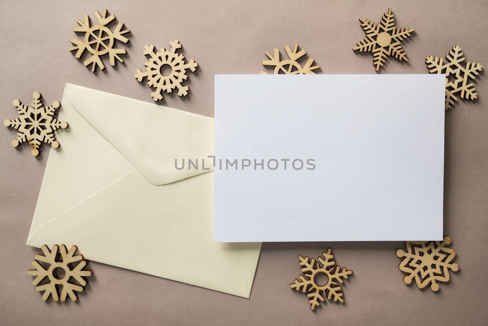Christmas winter festive ornament. Blank paper card with wooden snowflake on brown background. Minimal decoration. Invitation Christmas holiday party. Flat lay, top view, copy space.
