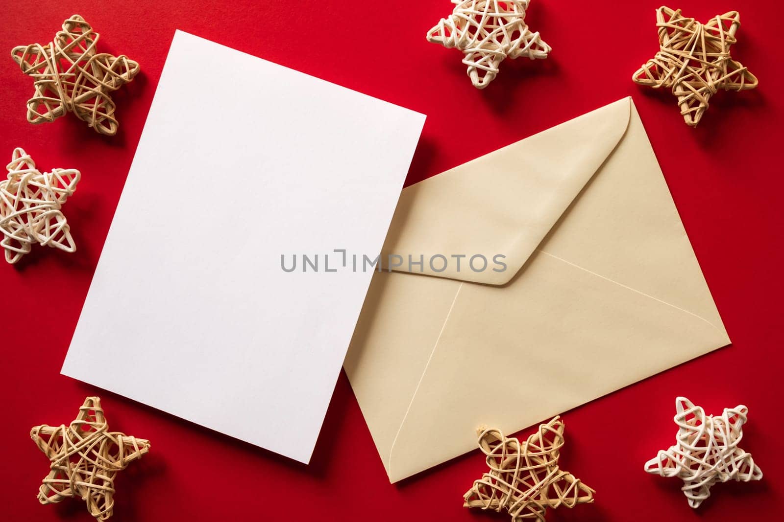Christmas winter festive ornament. Blank paper card and envelope with wooden decoration on red background. Minimal decoration. Invitation Christmas holiday party. Flat lay, top view, copy space.