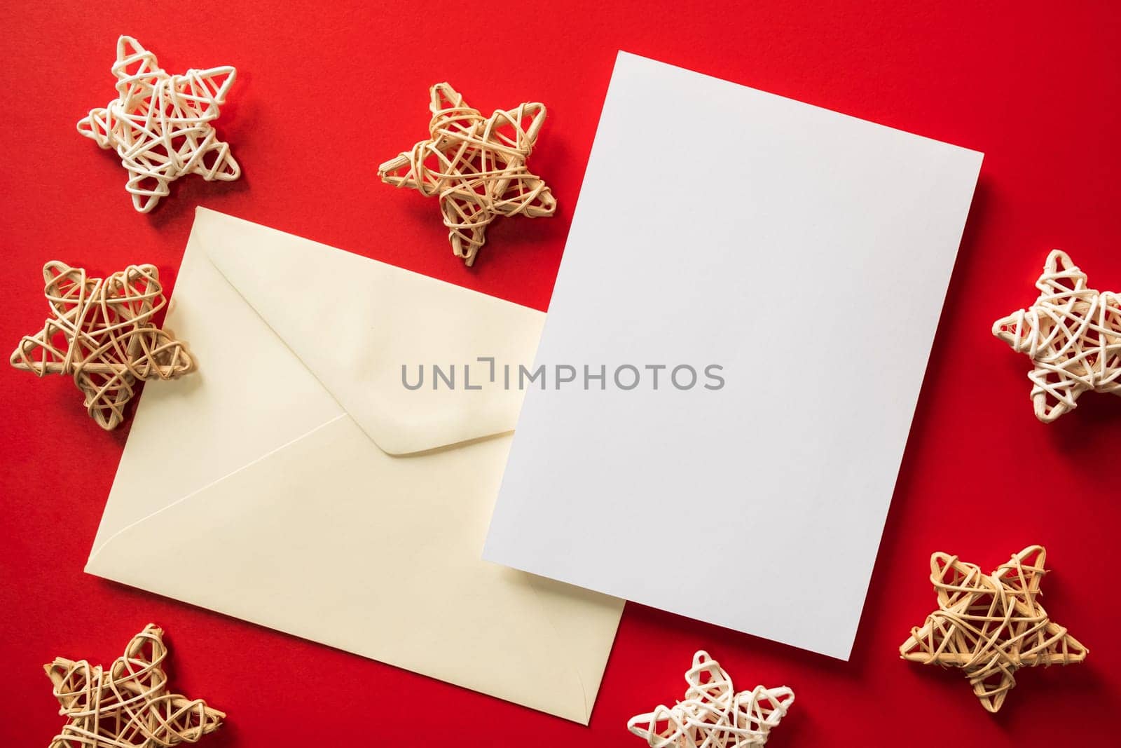 Christmas winter festive ornament. Blank paper card and envelope with wooden decoration on red background. Minimal decoration. Invitation Christmas holiday party. Flat lay, top view, copy space.