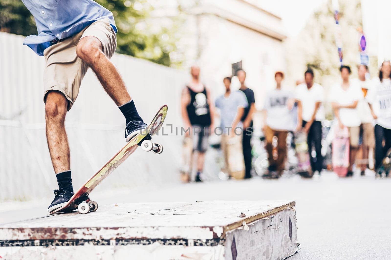 Young skateboarder skateboarding on the street. Skateboarding legs doing slide trick on object. Group of friends cheering in the background.