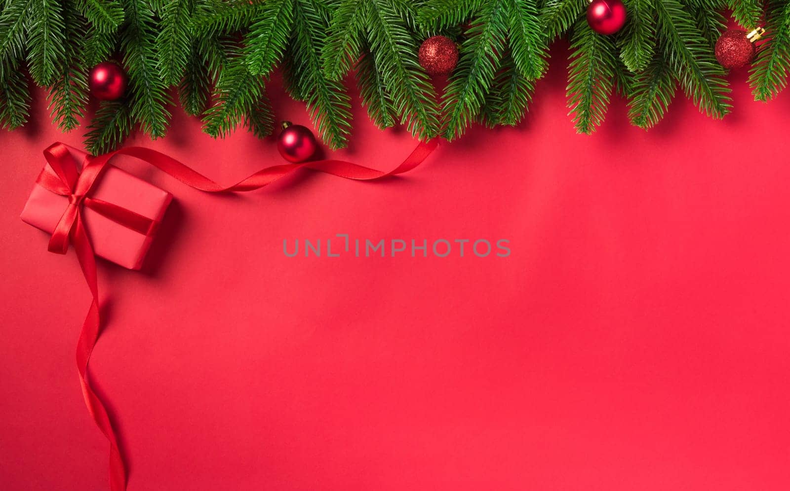 Christmas holiday background with gift box decorations composition, Top view fir green fir tree branches and Xmas ornaments on a red table background