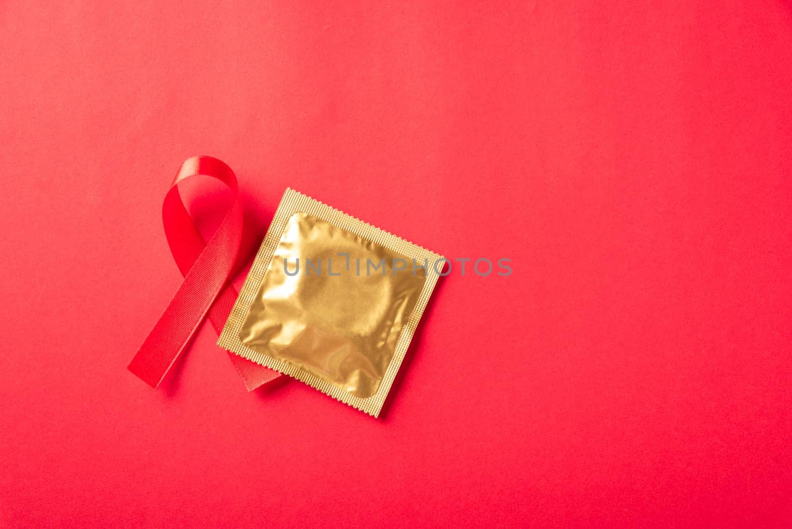 Red bow ribbon symbol HIV, AIDS cancer awareness and condom with shadows, studio shot isolated on red background, Healthcare medicine sexually concept, World AIDS Day