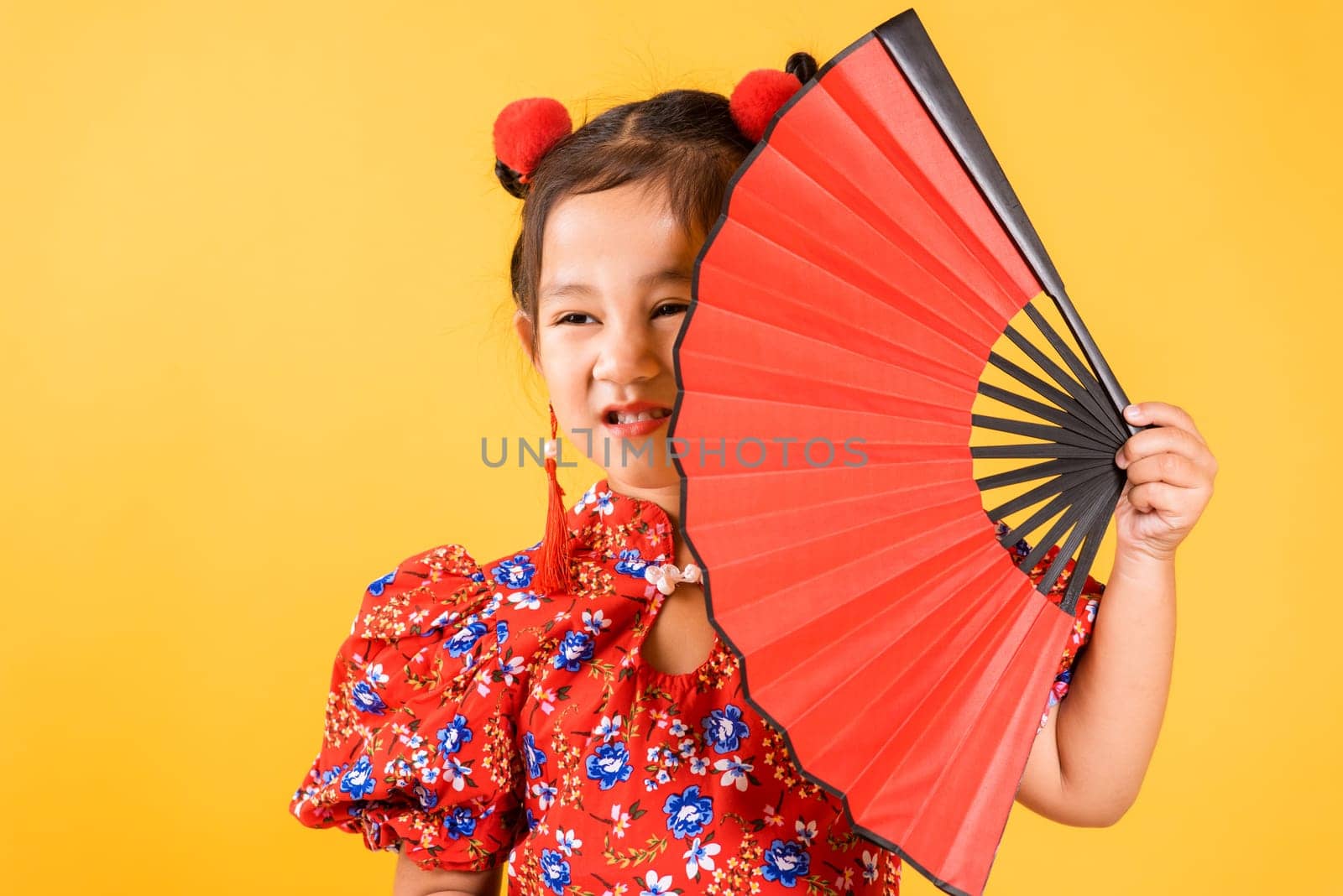 Chinese New Year. Happy Asian Chinese little girl smile wearing red cheongsam holding fan, Portrait children in traditional dress, studio short isolated on yellow background