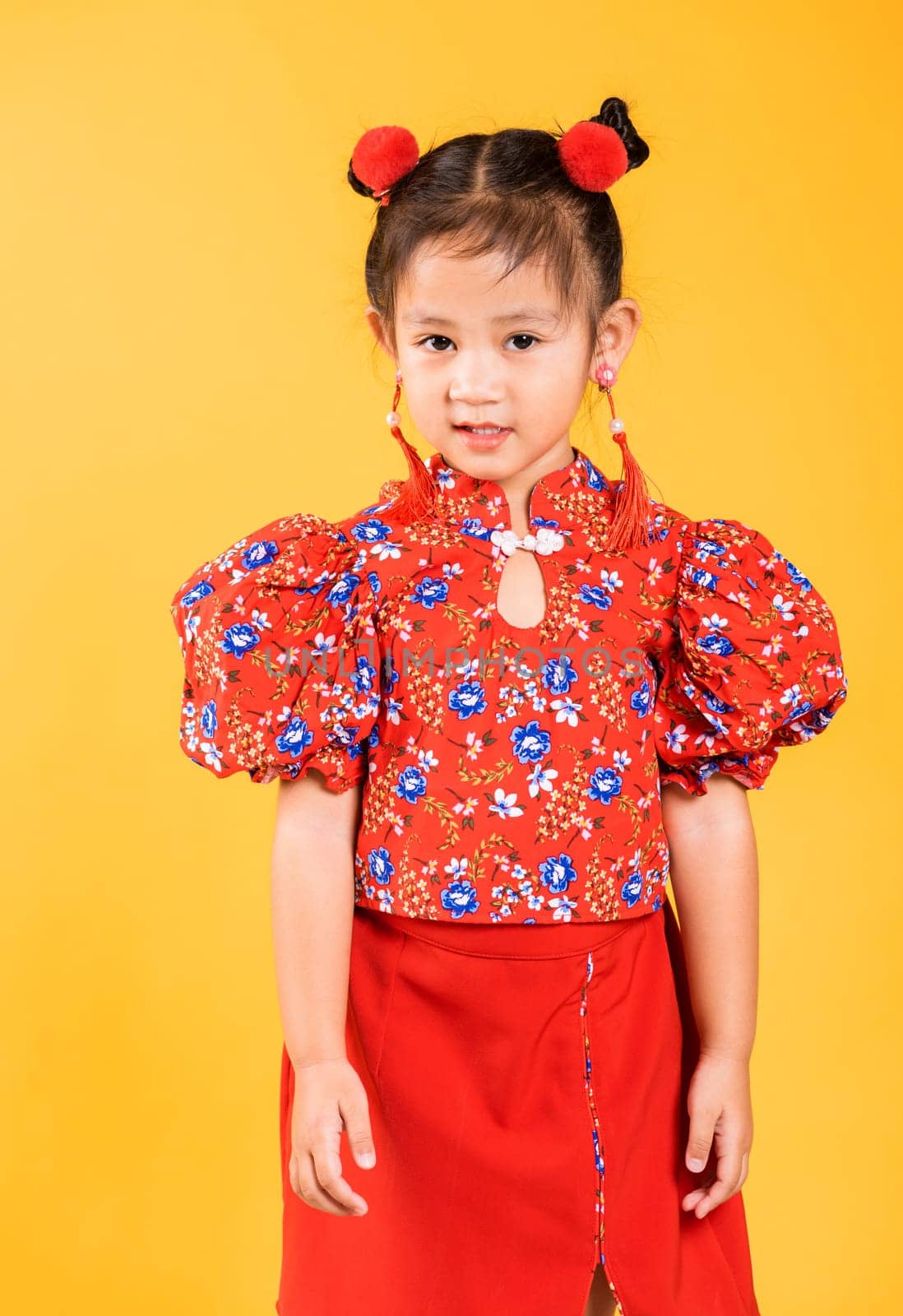 Happy Asian Chinese little girl smile wearing red cheongsam, Portrait children in traditional dress with greeting gesture celebration for Chinese New Year, studio short isolated on yellow background