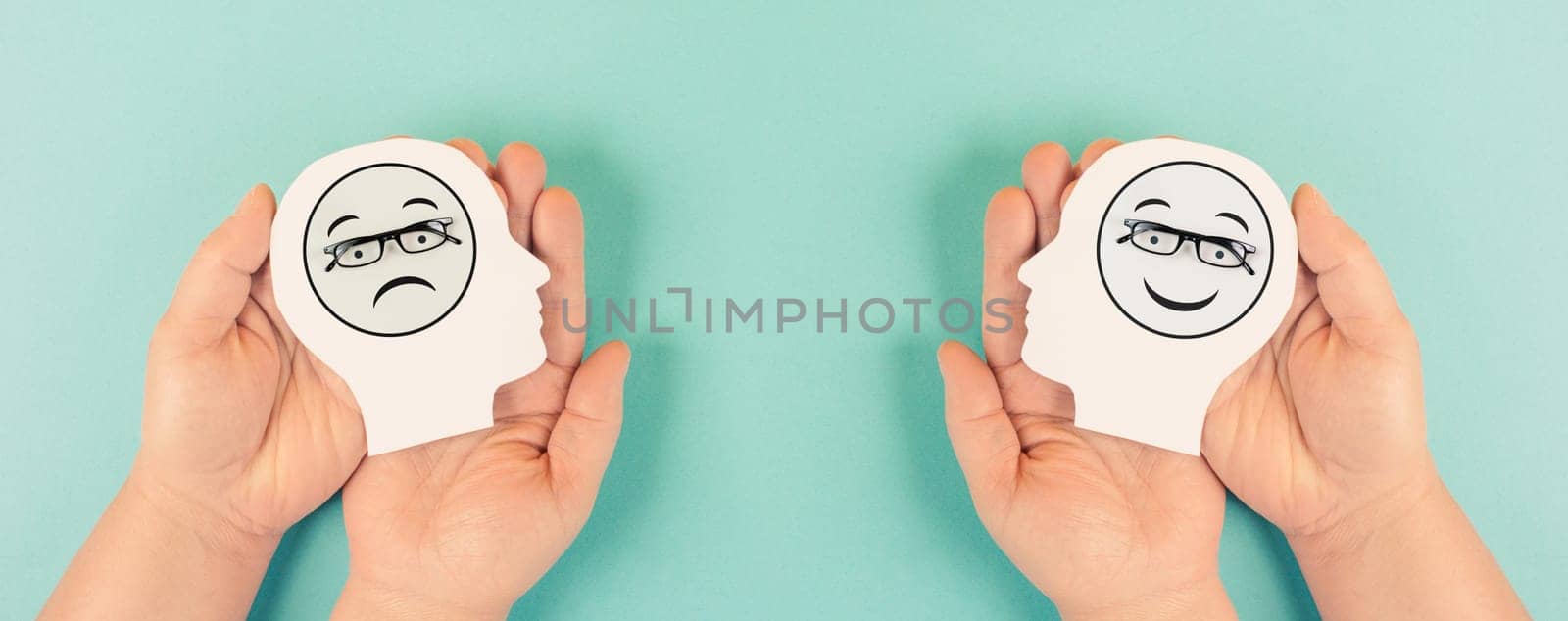 Holding a head with a sad and a happy face in the hands, mental health concept, positive and negative mindset, depression, support and evaluation symbol, emotion