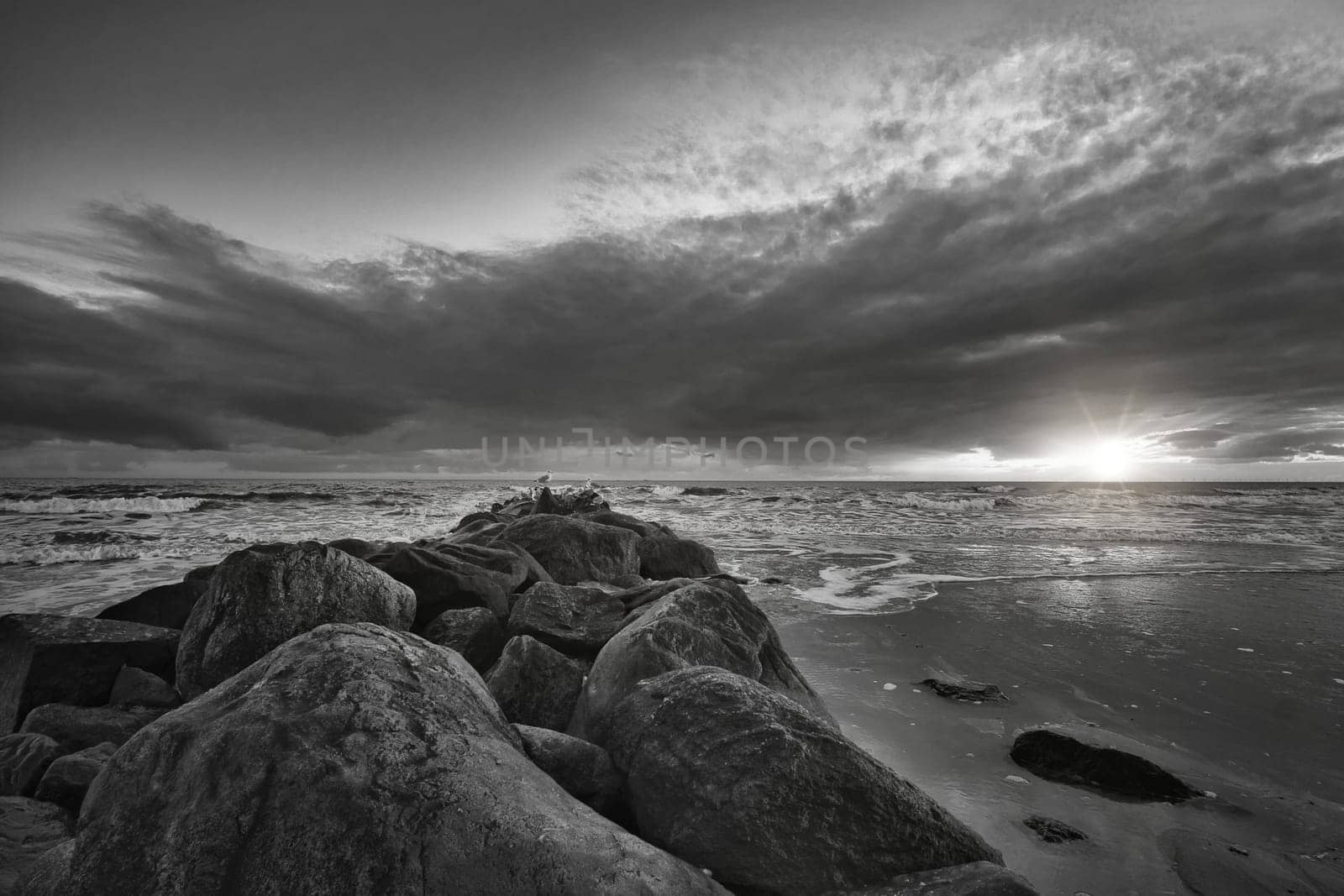 Sunset on the beach in Denmark taken in black and white. Stone groyne in the foreground. Walk on the coast in the sand. Landscape photo by the sea